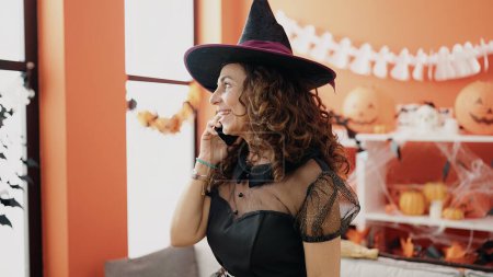 Foto de Mujer hispana de mediana edad hablando en smartphone teniendo fiesta de Halloween en casa - Imagen libre de derechos