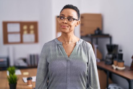 Téléchargez les photos : Femme afro-américaine travaillant au bureau portant des lunettes souriant regardant vers le côté et regardant loin en pensant. - en image libre de droit
