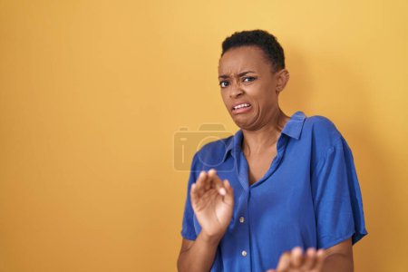 Téléchargez les photos : Femme afro-américaine debout sur fond jaune expression dégoûtée, mécontente et effrayée faisant face dégoût parce que réaction d'aversion. - en image libre de droit