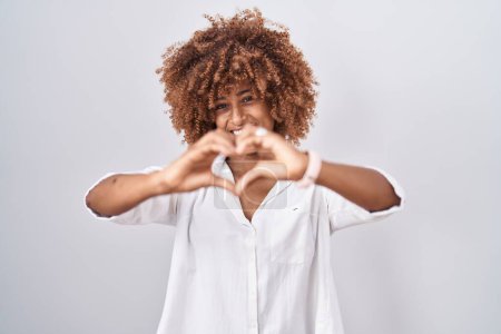 Photo for Young hispanic woman with curly hair standing over white background smiling in love doing heart symbol shape with hands. romantic concept. - Royalty Free Image
