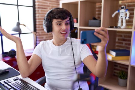 Téléchargez les photos : Jeune homme non binaire jouant à des jeux vidéo avec smartphone célébrant la réalisation avec un sourire heureux et l'expression gagnante avec la main levée - en image libre de droit