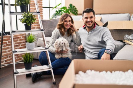 Photo for Young hispanic couple sitting on the floor at new home with log looking positive and happy standing and smiling with a confident smile showing teeth - Royalty Free Image
