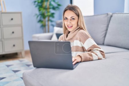 Young woman using laptop sitting on floor at home Poster 650006680