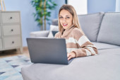 Young woman using laptop sitting on floor at home Poster #650006680