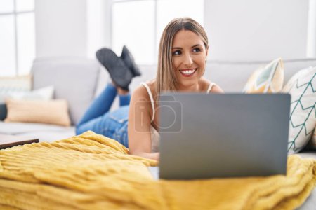 Téléchargez les photos : Young beautiful hispanic woman using laptop lying on table at home - en image libre de droit