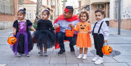 Téléchargez les photos : Homme hispanique et groupe d'enfants portant un costume d'Halloween souriant dans la rue - en image libre de droit