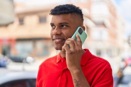Téléchargez les photos : Jeune homme latino souriant confiant parler sur le smartphone à la rue - en image libre de droit