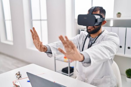 Téléchargez les photos : Jeune homme hispanique médecin utilisant des lunettes de réalité virtuelle à la clinique - en image libre de droit