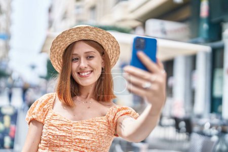 Foto de Joven mujer pelirroja turista con sombrero de verano hacer selfie por teléfono inteligente en la calle - Imagen libre de derechos