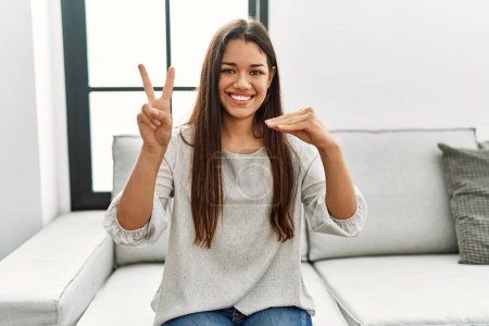 Téléchargez les photos : Jeune femme latine parlant avec la langue des signes assis sur le canapé à la maison - en image libre de droit