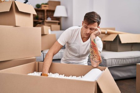 Photo for Young man unpacking cardboard box with unhappy expression at new home - Royalty Free Image