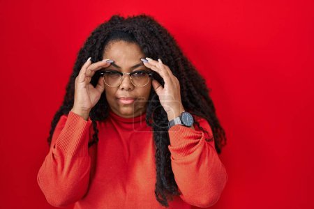 Photo for Plus size hispanic woman standing over red background trying to open eyes with fingers, sleepy and tired for morning fatigue - Royalty Free Image