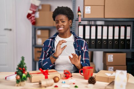 Photo for African american woman working at small business doing christmas decoration disgusted expression, displeased and fearful doing disgust face because aversion reaction. with hands raised - Royalty Free Image