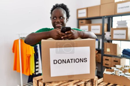 Téléchargez les photos : Jeune femme afro-américaine portant un uniforme bénévole en utilisant un smartphone au centre de charité - en image libre de droit