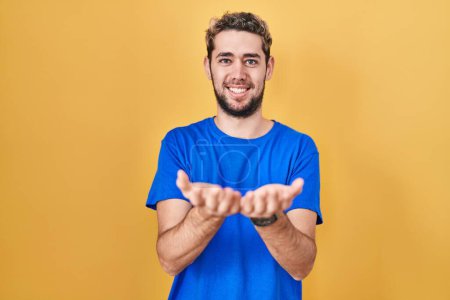 Téléchargez les photos : Homme hispanique avec la barbe debout sur fond jaune souriant avec les mains paumes ensemble recevant ou donnant geste. maintien et protection - en image libre de droit