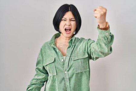 Téléchargez les photos : Jeune femme asiatique debout sur fond blanc en colère et fou levant le poing frustré et furieux tout en criant de colère. rage et concept agressif. - en image libre de droit