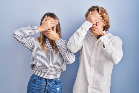 Photo for Young couple standing over blue background covering eyes and mouth with hands, surprised and shocked. hiding emotion - Royalty Free Image