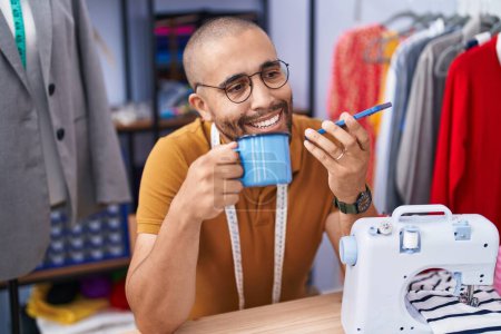 Téléchargez les photos : Jeune homme latin tailleur parler sur smartphone boire du café à l'atelier - en image libre de droit