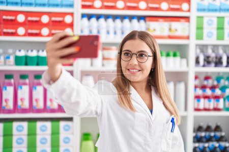 Téléchargez les photos : Young beautiful hispanic woman pharmacist smiling confident make selfie by smartphone at pharmacy - en image libre de droit