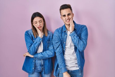 Photo for Young hispanic couple standing over pink background touching mouth with hand with painful expression because of toothache or dental illness on teeth. dentist - Royalty Free Image