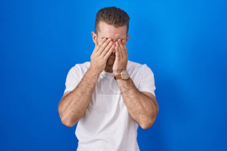 Photo for Young caucasian man standing over blue background rubbing eyes for fatigue and headache, sleepy and tired expression. vision problem - Royalty Free Image