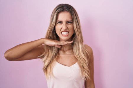 Photo for Young blonde woman standing over pink background cutting throat with hand as knife, threaten aggression with furious violence - Royalty Free Image