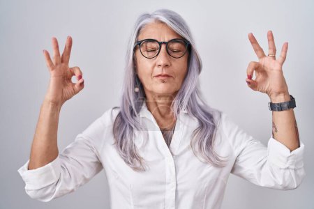 Téléchargez les photos : Femme d'âge moyen avec des tatouages portant des lunettes debout sur fond blanc se détendre et sourire avec les yeux fermés faire geste de méditation avec les doigts. concept de yoga. - en image libre de droit