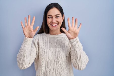 Photo for Young brunette woman standing over blue background showing and pointing up with fingers number ten while smiling confident and happy. - Royalty Free Image