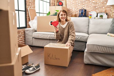 Téléchargez les photos : Young caucasian woman smiling confident packing kitchen package at new home - en image libre de droit