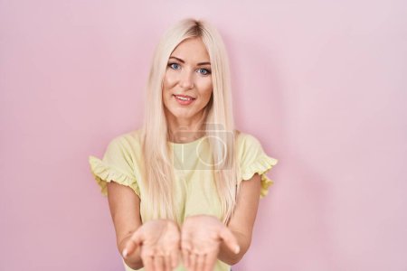 Foto de Mujer caucásica de pie sobre fondo rosa sonriendo con las palmas de las manos juntas recibiendo o dando gesto. retención y protección - Imagen libre de derechos