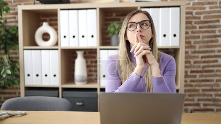 Téléchargez les photos : Jeune femme blonde travailleur d'affaires en utilisant un ordinateur portable avec l'expression du doute au bureau - en image libre de droit
