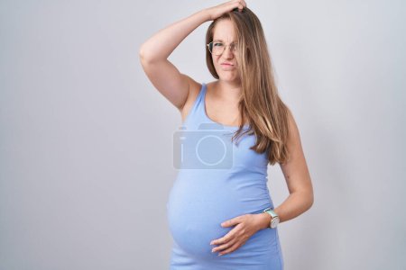 Téléchargez les photos : Jeune femme enceinte debout sur fond blanc confondre et se poser des questions. incertain avec doute, pensant la main sur la tête. concept coûteux. - en image libre de droit