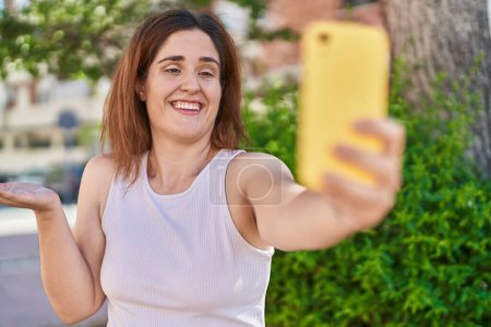 Téléchargez les photos : Femme brune prenant une photo selfie avec smartphone célébrant la réalisation avec sourire heureux et expression gagnante avec la main levée - en image libre de droit