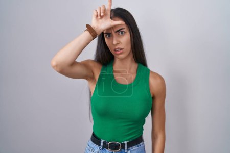Photo for Young woman standing over isolated background making fun of people with fingers on forehead doing loser gesture mocking and insulting. - Royalty Free Image