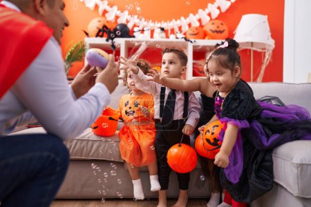 Foto de Hombre hispano y grupo de niños teniendo fiesta de Halloween jugando con burbujas sopa en casa - Imagen libre de derechos