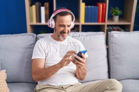Foto de Middle age man listening to music sitting on sofa at home - Imagen libre de derechos
