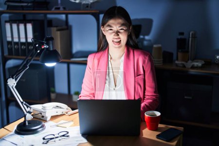 Foto de Mujer joven china que trabaja en la oficina por la noche sacando la lengua feliz con expresión divertida. concepto de emoción. - Imagen libre de derechos
