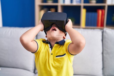 Foto de Adorable niño hispano jugando videojuego usando gafas de realidad virtual en casa - Imagen libre de derechos