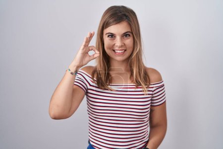 Foto de Mujer hispana joven de pie sobre un fondo aislado sonriendo positiva haciendo signo de ok con la mano y los dedos. expresión exitosa. - Imagen libre de derechos
