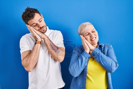 Photo for Young brazilian mother and son standing over blue background sleeping tired dreaming and posing with hands together while smiling with closed eyes. - Royalty Free Image