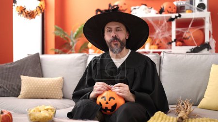 Téléchargez les photos : Jeune homme chauve portant costume de sorcier tenant doux de citrouille panier d'Halloween à la maison - en image libre de droit