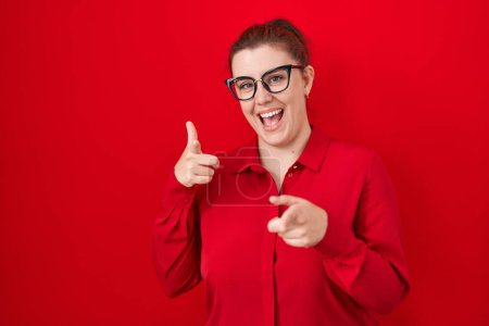 Photo for Young hispanic woman with red hair standing over red background pointing fingers to camera with happy and funny face. good energy and vibes. - Royalty Free Image