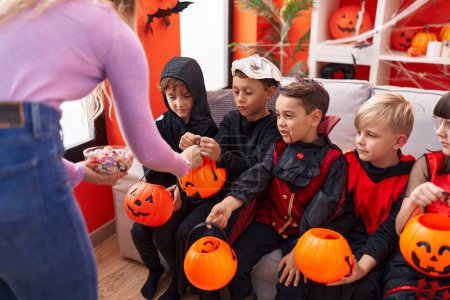 Foto de Grupo de niños con disfraz de halloween recibiendo caramelos en canasta de calabaza en casa - Imagen libre de derechos
