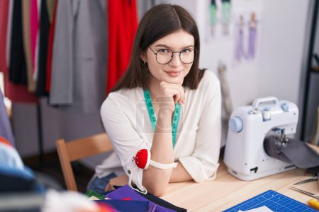 Téléchargez les photos : Young caucasian woman tailor smiling confident sitting on table at tailor shop - en image libre de droit