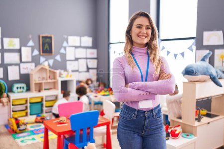 Photo for Young blonde woman teacher smiling confident standing with arms crossed gesture at kindergarten - Royalty Free Image