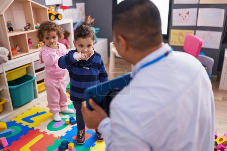 Photo for Hispanic man with boy and girl having lesson using touchpad at kindergarten - Royalty Free Image