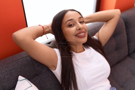 Photo for Young arab woman relaxed with hands on head sitting on sofa at home - Royalty Free Image