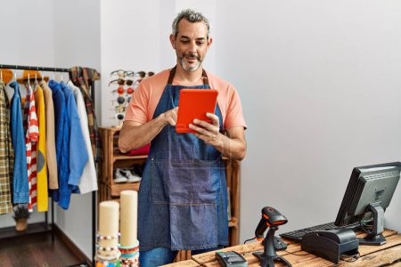 Foto de Asistente de tienda de hombre de pelo gris de mediana edad usando touchpad en la tienda de ropa - Imagen libre de derechos