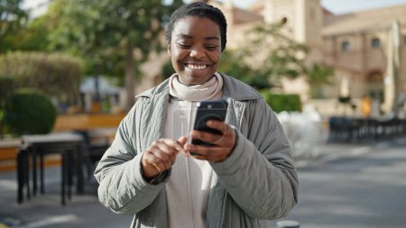 Foto de Mujer afroamericana usando smartphone sonriendo en el parque - Imagen libre de derechos