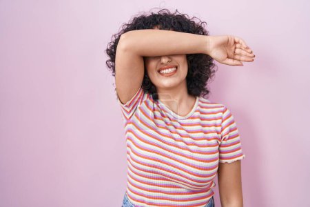 Foto de Joven mujer de Oriente Medio de pie sobre fondo rosa cubriendo los ojos con el brazo sonriendo alegre y divertido. concepto ciego. - Imagen libre de derechos